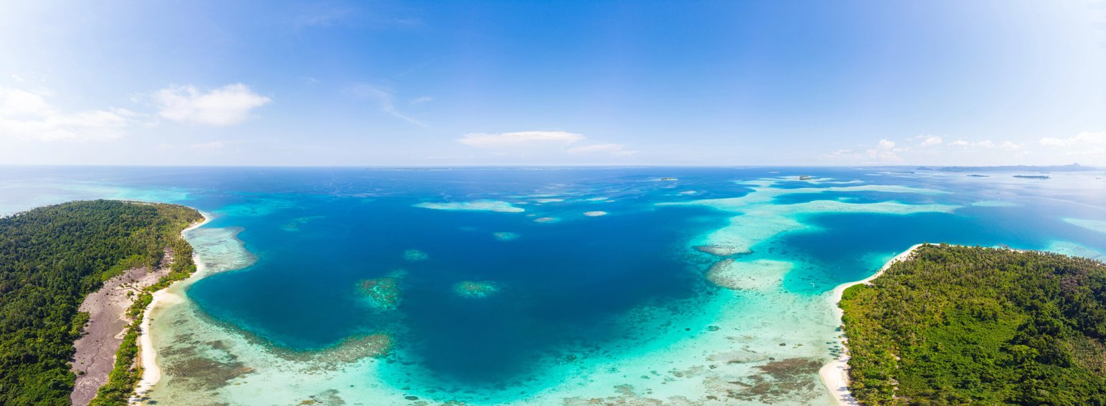 Aerial view of turquoise Caribbean water, coral reefs, and green islands under a clear blue sky.